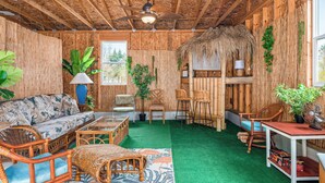 A room with a thatched roof, bamboo walls, and a green artificial turf floor. There are wicker furniture pieces, including a sofa, chairs, and a table. - Tiki Bar! Near wineries, Sleeping Bear Dunes, TC - Cedar Cottage (Cedar)