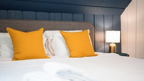 A neatly made bed with white linens and two bright orange pillows, a wooden headboard, and a bedside lamp. - Tiki Bar! Near wineries, Sleeping Bear Dunes, TC - Cedar Cottage (Cedar)