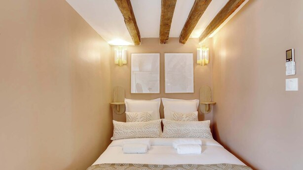 Habitación de hotel con cama, cabecero, luces fijadas en la pared y un termostato.