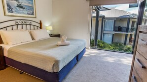 A hotel room with a bed, a nightstand, a lamp, and a view of the outside balcony.