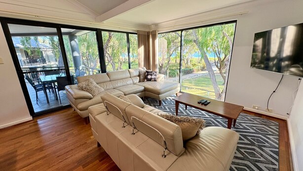 A spacious living room with a large sectional sofa, a coffee table, and a TV mounted on the wall.