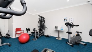 Een fitnessruimte met trainingsapparatuur, een rode trainingsbal en een blauw tapijt.