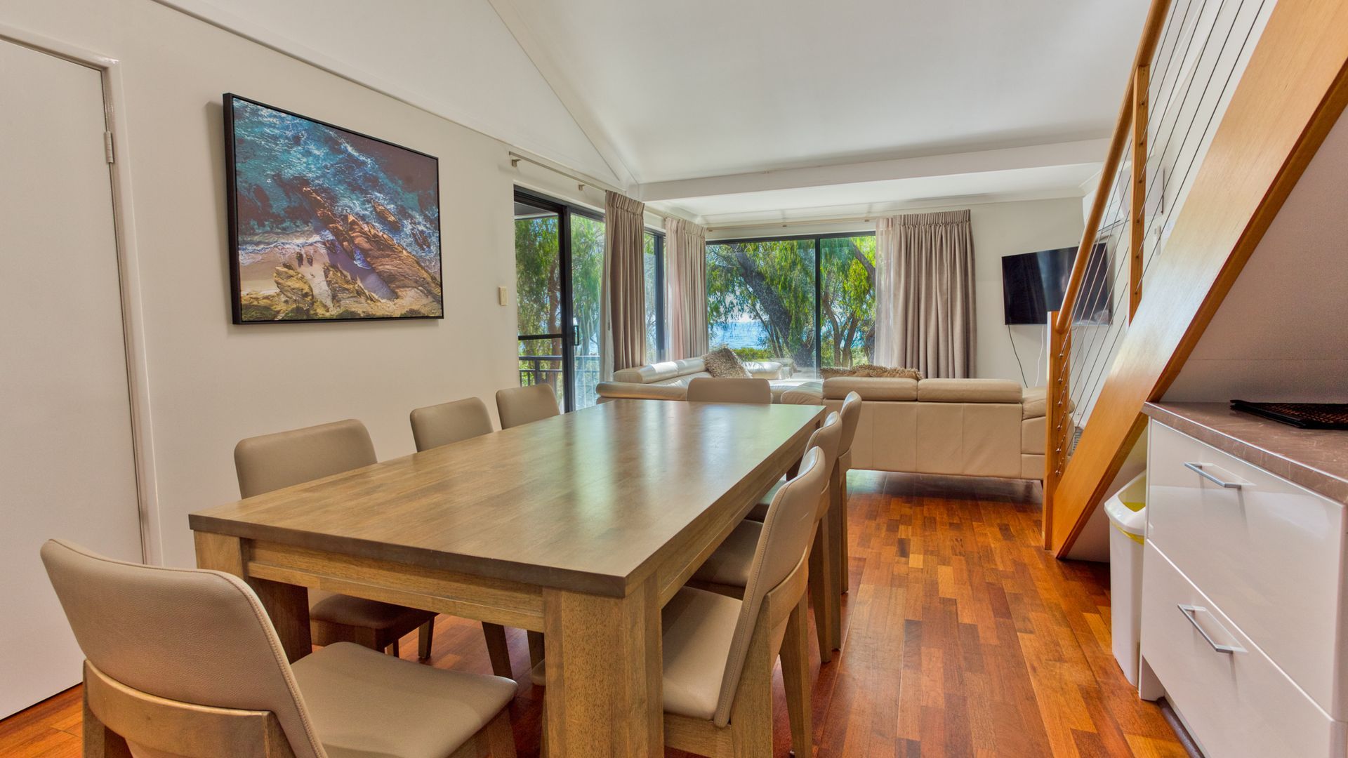 A modern dining area with a wooden table and chairs, a sofa, and a television.