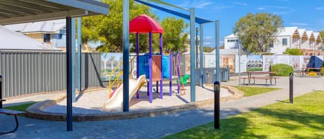 Un parque infantil con tobogán, estructuras para escalar y una zona de juegos cubierta.