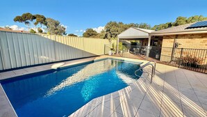 A swimming pool with a tiled deck, a covered seating area, and a fenced garden.