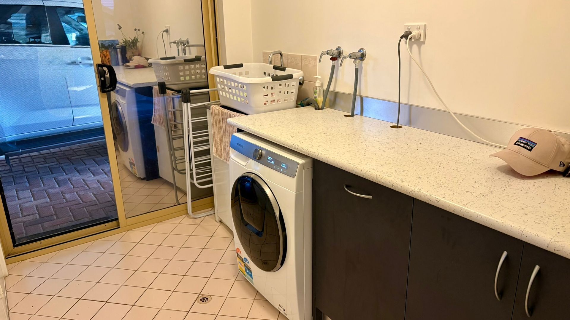 Une buanderie équipée d’un lave-linge à chargement frontal, d’un étendoir, d’un panier et d’un évier avec un tuyau.