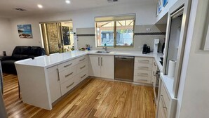 A modern kitchen with white cabinetry, a built-in dishwasher, and a window overlooking a garden.