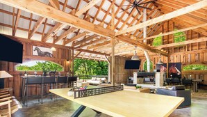 Un grand espace intérieur comprenant une table de ping-pong, des poutres en bois et un coin bar avec des sièges.