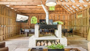 Un intérieur rustique en bois, agrémenté d’une cheminée en pierre, d’un coin salon et d’un téléviseur diffusant des images d’un paysage montagneux.