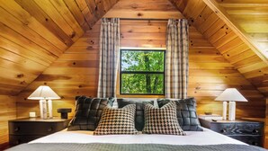 Une chambre confortable dans un chalet en bois, avec un grand lit, deux tables de chevet et une fenêtre agrémentée de rideaux à carreaux.