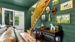 Une pièce chaleureuse avec un escalier en bois, un banc en bois, une table agrémentée d’objets décoratifs et des tableaux encadrés accrochés au mur.