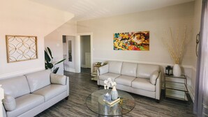 A living room with two sofas, a coffee table, a painting, and a vase with branches.