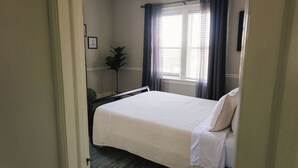 A bedroom with a bed, a window with curtains, a plant, and a ceiling light.
