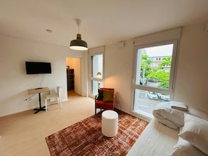Een moderne hotelkamer met een flatscreen televisie, een bureau, een comfortabele fauteuil, een bank, een groot raam met uitzicht op de stad en een kamerbreed tapijt met een patroon.