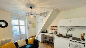 A compact living space with a black leather sofa, a glass coffee table, a kitchen with white cabinets, and a dining area with stools. - La Suite Marie Stuart Hypercentre (Reims)