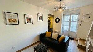 A living room with a black sofa, a glass coffee table, and framed artwork on the wall. - La Suite Marie Stuart Hypercentre (Reims)