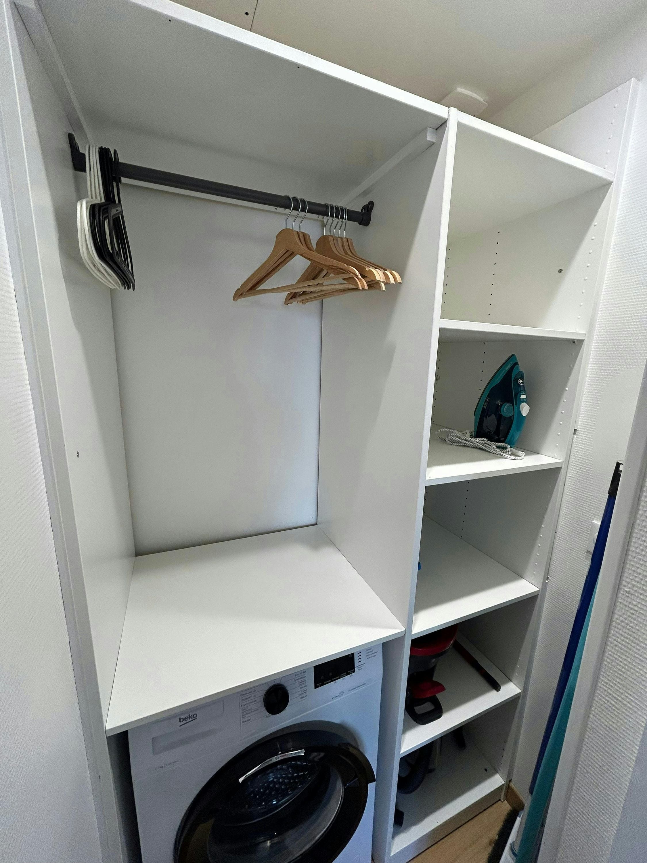 A laundry area with a washing machine, a drying rack, and shelves for storage.