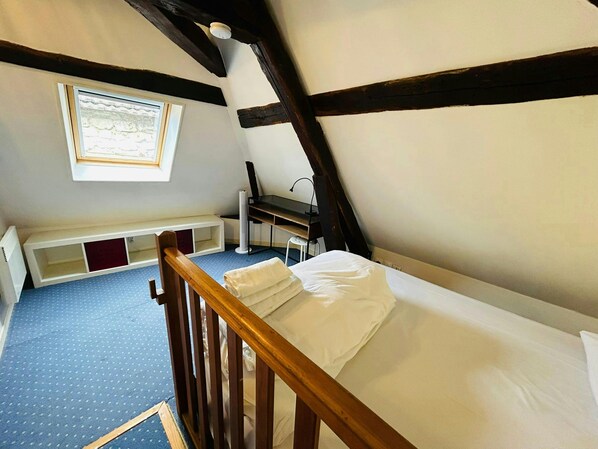 Une chambre avec un plafond en pente, un lit en bois, un bureau et une fenêtre.