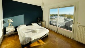 Une chambre à coucher avec un lit, des tables de chevet, une lampe et une vue sur la ville grâce à de grandes fenêtres.