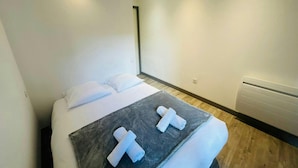 Une chambre moderne avec un lit, des oreillers blancs, une couverture grise et deux serviettes enroulées.