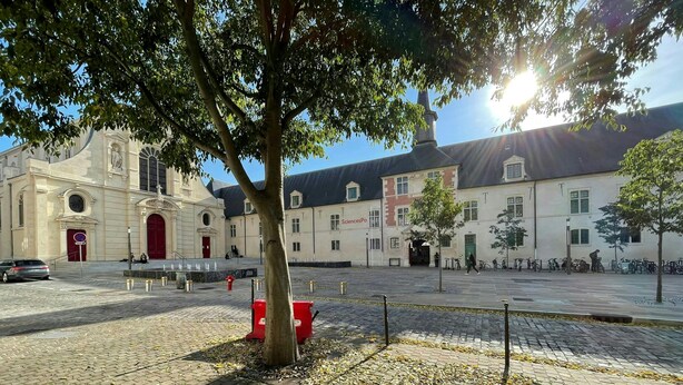 Une cour dallée de pierres, un arbre et un bâtiment avec une porte rouge.