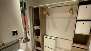 Une petite buanderie équipée d’un lave-linge à chargement frontal, d’un sèche-linge et d’un meuble de rangement intégré, doté d’étagères et d’un espace pour suspendre le linge.