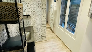Un couloir étroit avec un mur carrelé, une étagère noire avec des paniers, un petit lavabo et une fenêtre donnant sur un paysage agréable.
