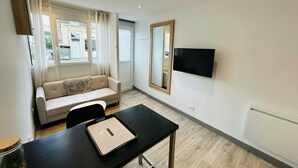 Un salon moderne avec un canapé, une table à manger sur laquelle se trouve un plateau, un téléviseur fixé au mur et une fenêtre avec des rideaux.