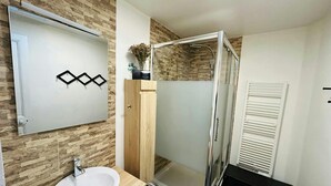 A modern bathroom with a glass shower enclosure, a wooden vanity with a sink, and a mirror with a geometric decoration. - Le Charmant Carnot Cath Drale (Reims)