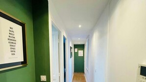 A narrow hallway with green walls, wooden flooring, and white trim. There is a framed sign on the left wall and a thermostat on the right wall. - Le Charmant Carnot Cath Drale (Reims)