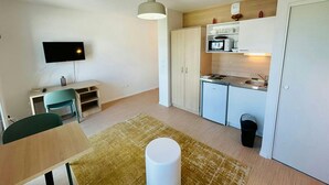 Un espace de vie compact comprenant un coin cuisine, un coin repas et un téléviseur fixé au mur.