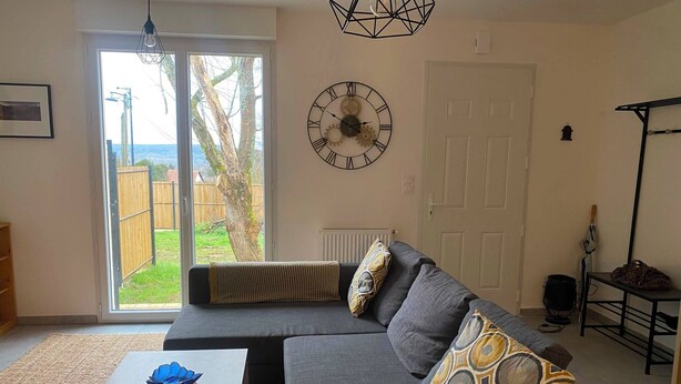 A living room with a sectional sofa, a coffee table, a wall clock, and a view through a glass door. - "La clé des champs" Vacation Rental (Bueil)