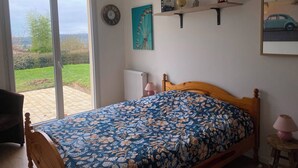 A bedroom with a bed, a window, a wall clock, a shelf with decorative items, and a painting. - "La clé des champs" Vacation Rental (Bueil)