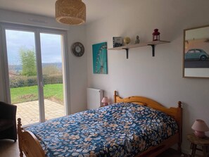 A bedroom with a bed, a window, a wall clock, a shelf with decorative items, and a painting. - "La clé des champs" Vacation Rental (Bueil)