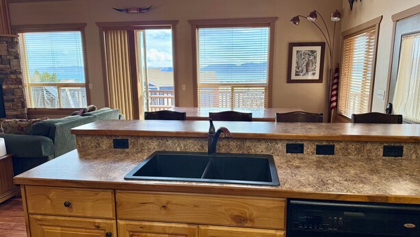 A kitchen with a granite countertop, a built-in dishwasher, and a large window overlooking a balcony. - Rustic Mountain Lake Escape (Garden City)