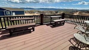 A wooden deck with picnic tables and chairs, overlooking a scenic landscape with mountains and a body of water. - Rustic Mountain Lake Escape (Garden City)