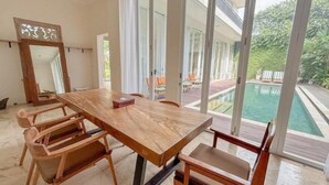 Une pièce spacieuse avec une grande table et des chaises en bois, de grandes fenêtres et une vue sur une piscine.