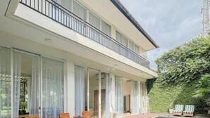 Un bâtiment moderne à deux étages doté d’une piscine, d’une terrasse en bois et d’un espace extérieur aménagé pour s’asseoir.