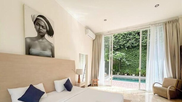 Une chambre d’hôtel avec un grand lit, un tableau au mur et une vue sur une piscine et la verdure environnante.