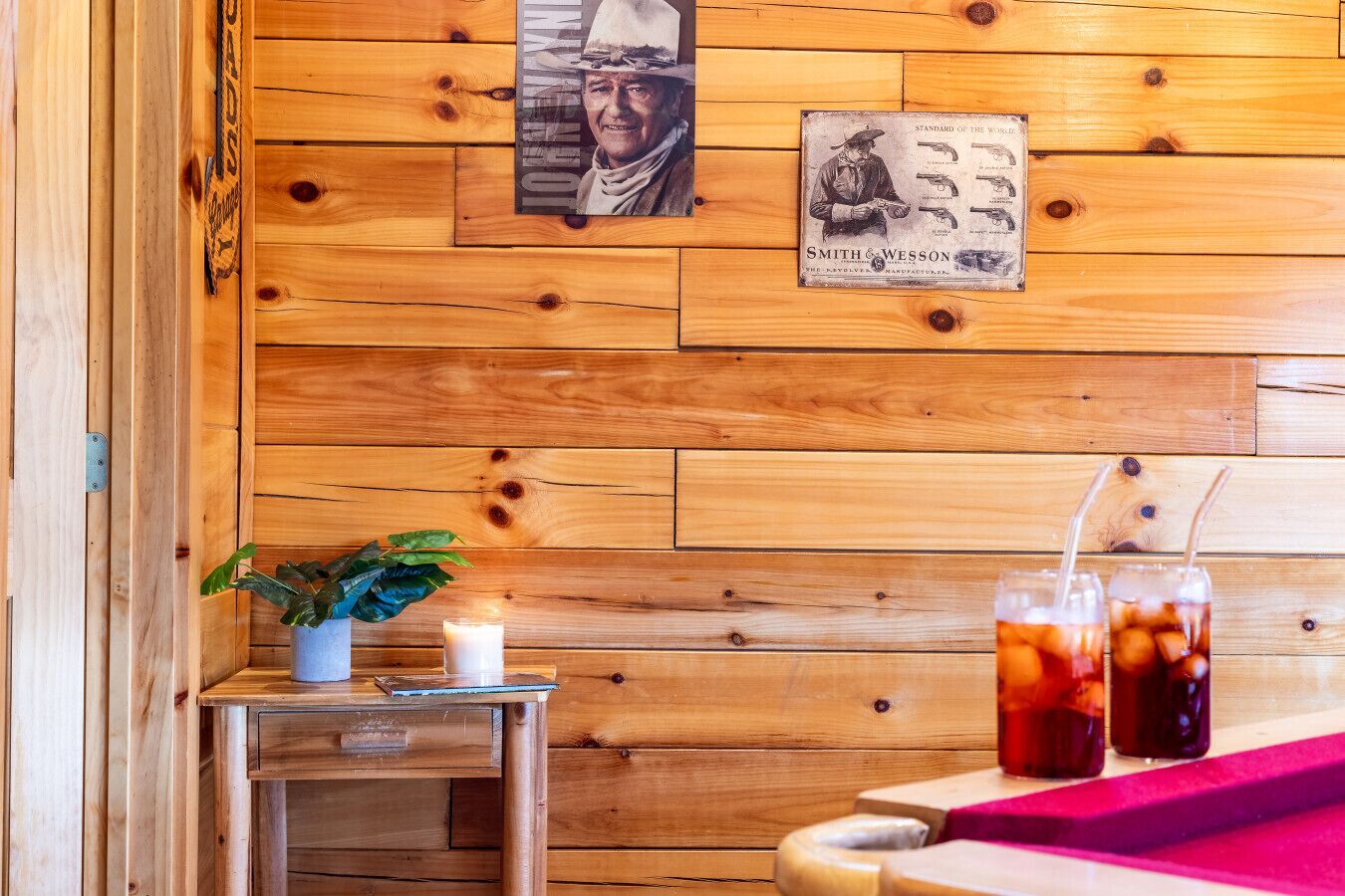 Un mur en bois orné de tableaux encadrés, une petite table avec une plante, une bougie et deux boissons.