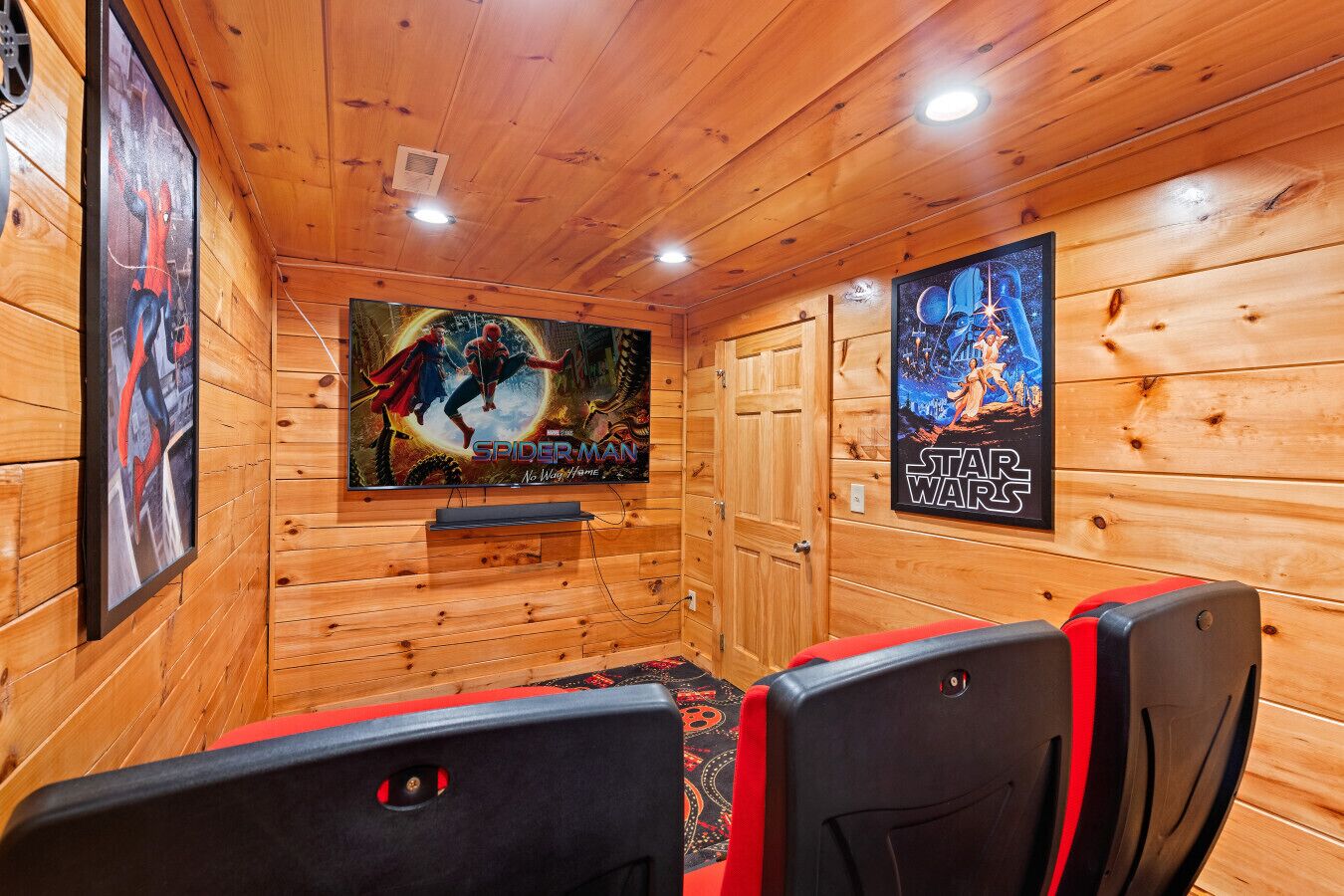 Ein Zimmer mit Holzvertäfelung, einem großen Flachbildfernseher an der Wand, zwei roten und schwarzen Gaming-Stühlen und Postern von Spider-Man und Star Wars.