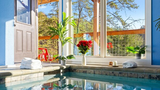 A pool area with a clear view of the surrounding landscape, a wooden pergola, and a window with a view of trees and a fence.