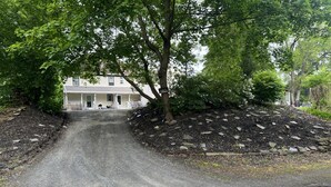Une allée menant à une maison dotée d’un porche, entourée d’arbres et d’un espace paysager agrémenté de rochers.