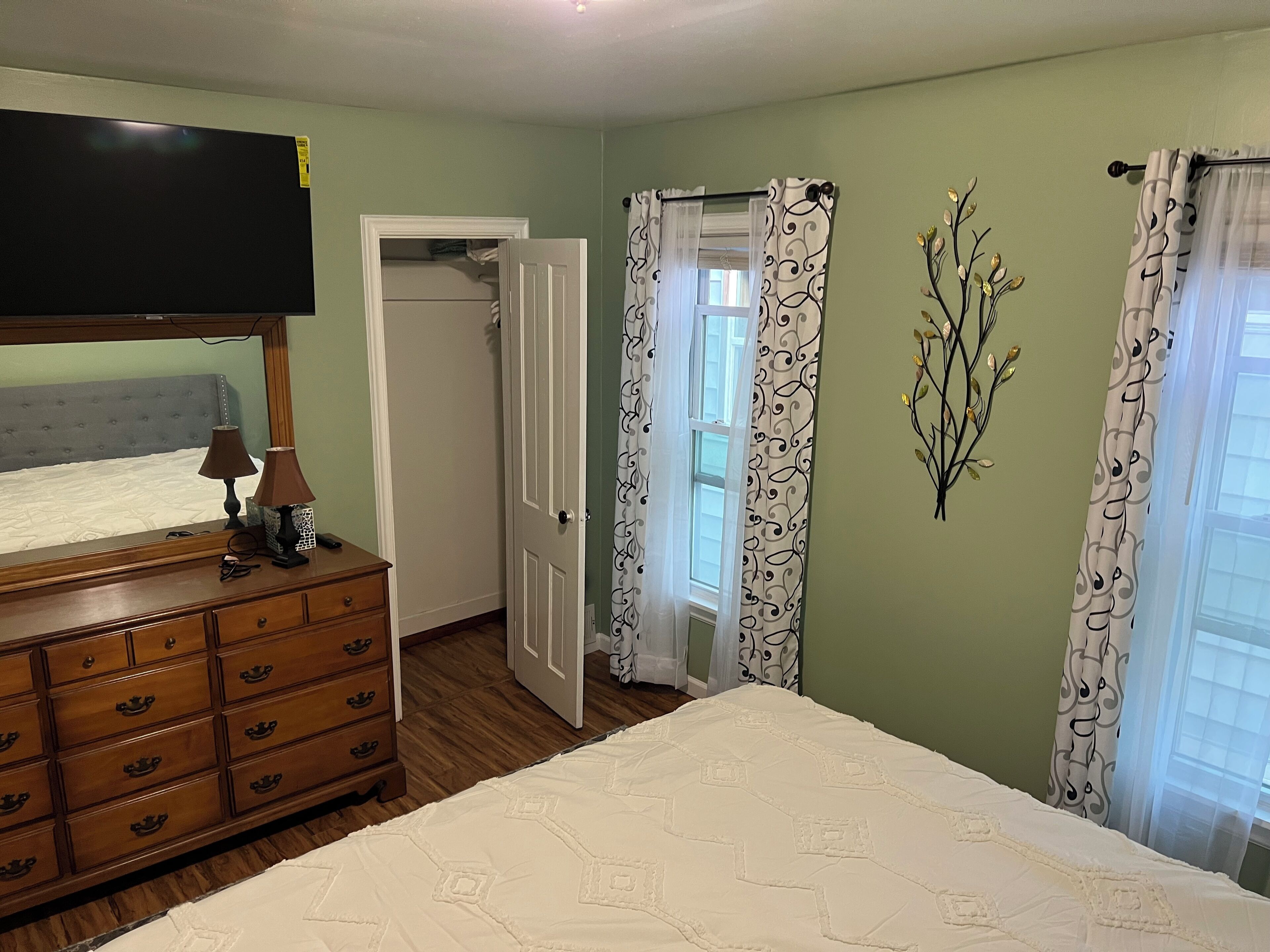 Um quarto com cama, cômoda e televisão na parede.