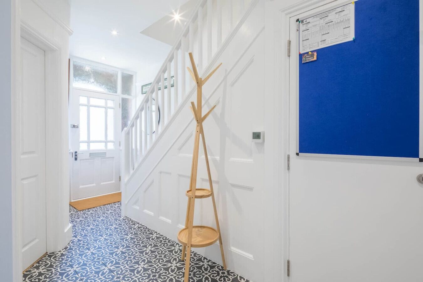 A hallway with patterned flooring, a wooden ladder, a blue bulletin board, and a staircase.