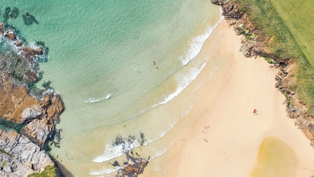 An aerial view of a beach with clear waters, rocky coastline, and a few people.