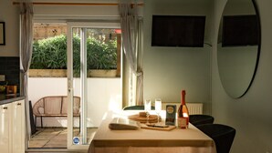 A dining area with a table set for two, a bottle of wine, and a television mounted on the wall.