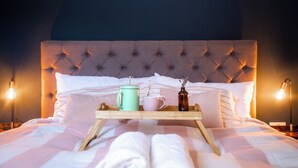 A neatly made bed with a tray of breakfast items, including a mug, a cup, and a bottle, set against a tufted headboard.