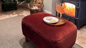 A cozy living room with a red ottoman, a Christmas tree, and a wood-burning stove.