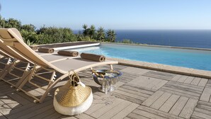 A poolside area with lounge chairs, a glass bowl with a bottle, and a woven basket. - Coastline Arrabida Villa by Cadenzalux (Sesimbra)